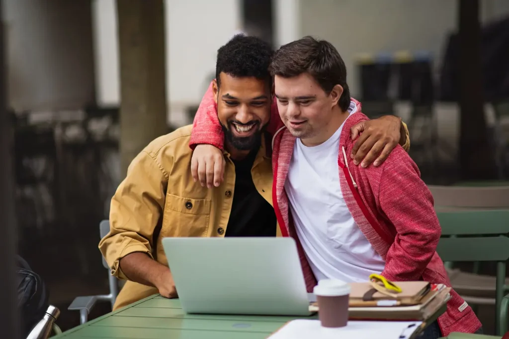 Disabled man and support worker smiling while looking at computer