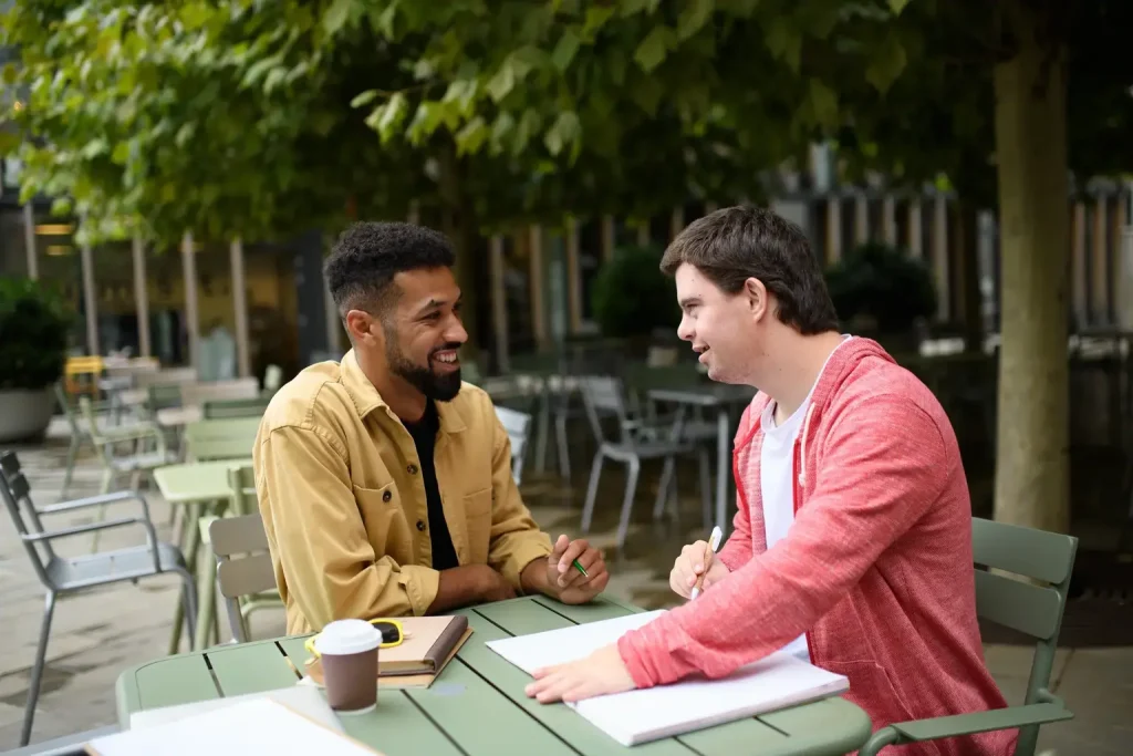 Disabled man and support worker talking at a cafe